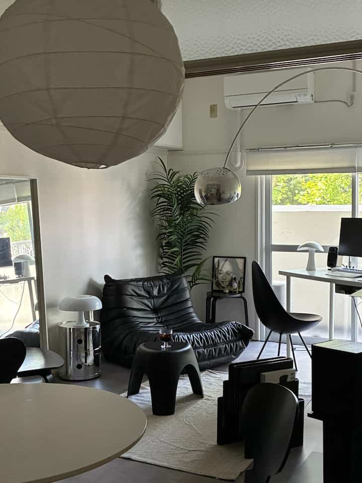 Monotone living room for a single household featuring a black leather lounge chair, floor lamp, and a work desk with a computer, creating a simple and stylish atmosphere