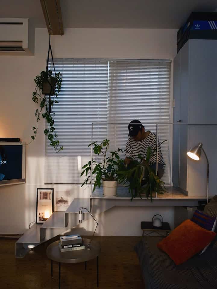 ナチュラルな色調の1LDKリビング、植物が多く配置され、ソファやコーヒーテーブル、フロアランプがある雰囲気のある空間