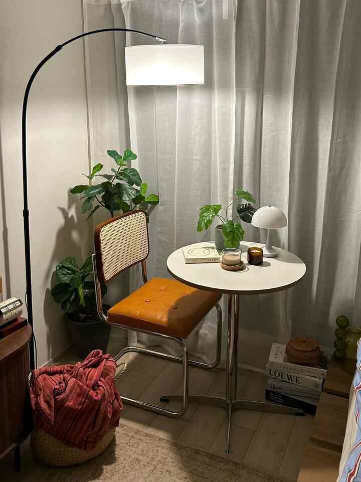ホワイトとブラウンのトーンでまとめられた小さな部屋、円形テーブルとラタンチェア、フロアランプと植物が配置された雰囲気あるカフェ風インテリア