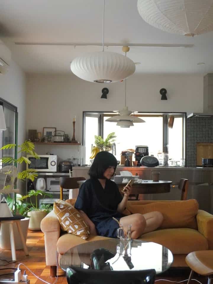 Natural tone living room featuring a mustard-colored sofa, wooden flooring, and various plants creating a cozy atmosphere