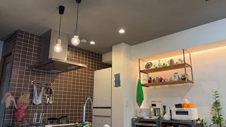A narrow modern kitchen with white walls and brown tiled backsplash featuring pendant lights as focal points and a clean, organized layout