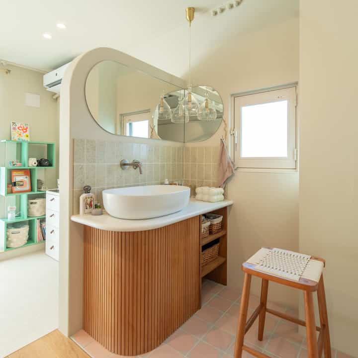 Bright beige and white bathroom featuring natural wood stool and clean sink area with a relaxed atmosphere