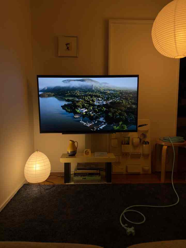 Warm yellow-lit white-walled living room featuring centered TV and floor lamp on bottom left