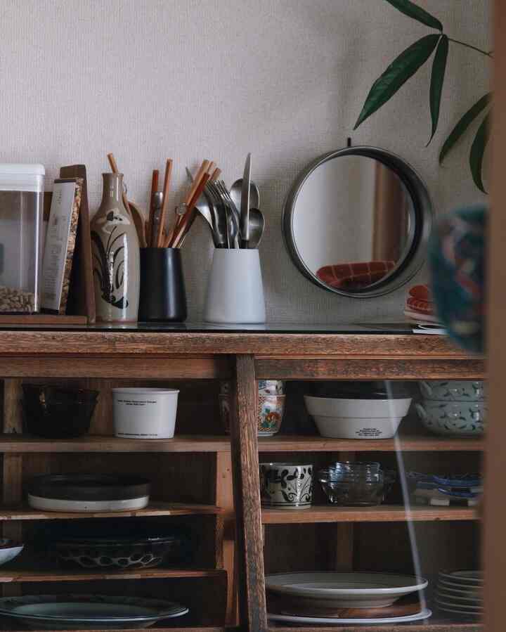 Natural kitchen space featuring a light brown wooden storage cabinet, assorted dishware, a round mirror, and green plant leaves in the top right corner