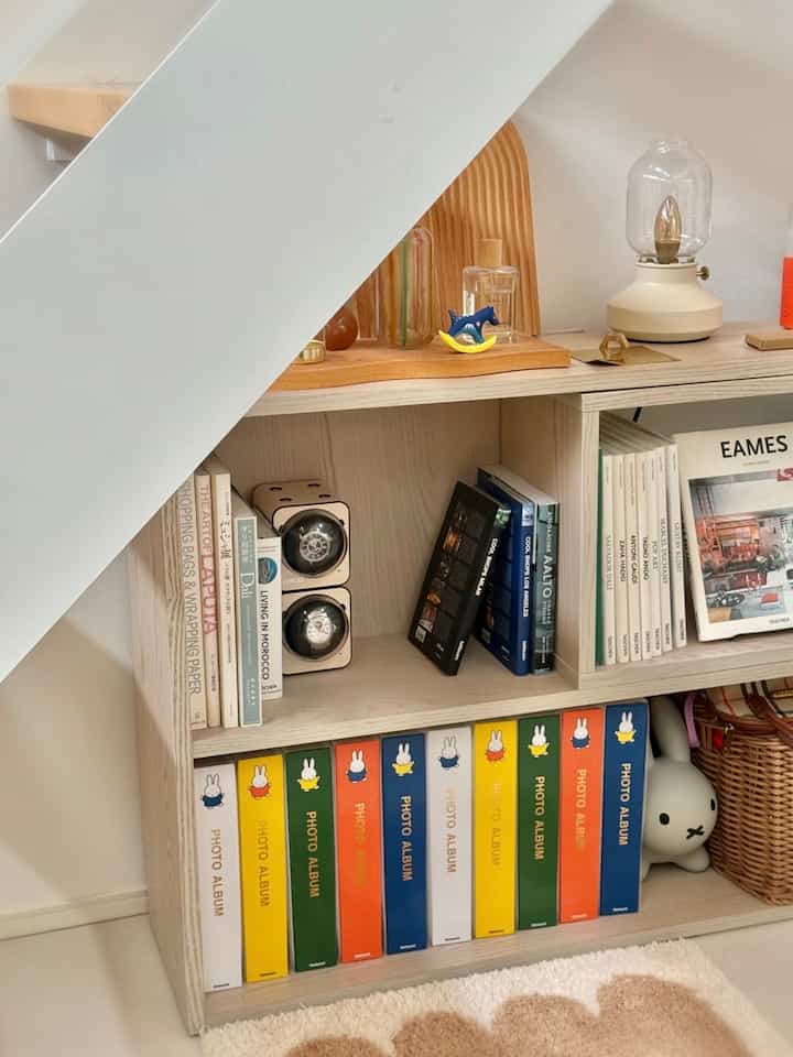 White-toned space under stairs featuring brown wooden shelves with books and decorative items, creating a cozy and organized storage area