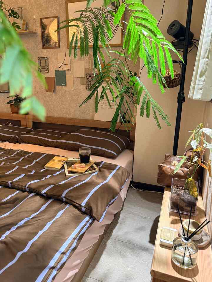 ブラウンを基調とした寝室、ストライプのベッドカバーと室内植物が配置された雰囲気のある空間