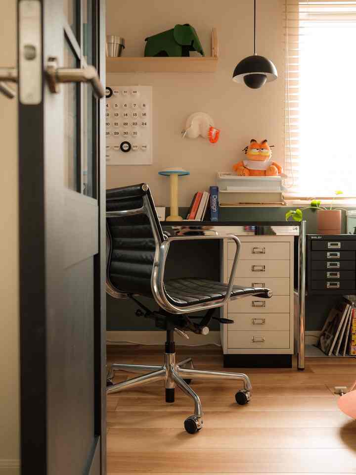 Mid-Century Modern home office featuring black office chair and white desk with warm wooden flooring and soft natural light