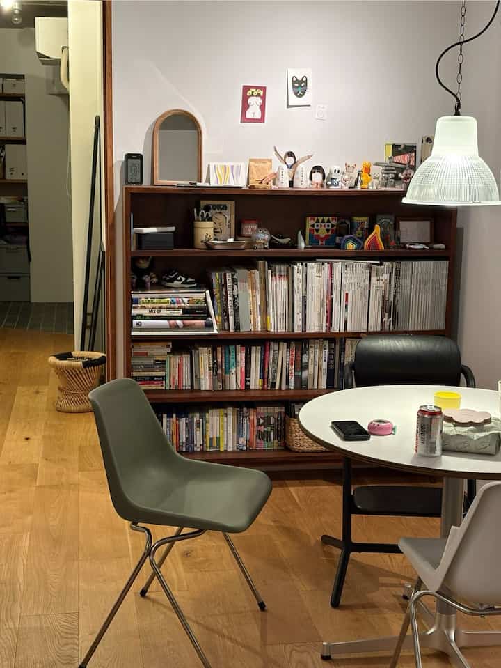 白い壁と木目調の本棚、丸テーブルと椅子が配置された、ナチュラルでヴィンテージ感のあるダイニングスペース