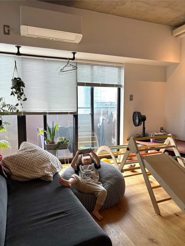 Natural wood tone modern living room featuring a child on bean bag sofa, window blinds, and plants creating a cozy atmosphere