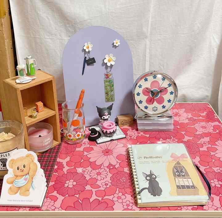 ピンクの花柄テーブルランナーの上にレトロな時計とキャンドルが置かれた居心地の良いワークスペース