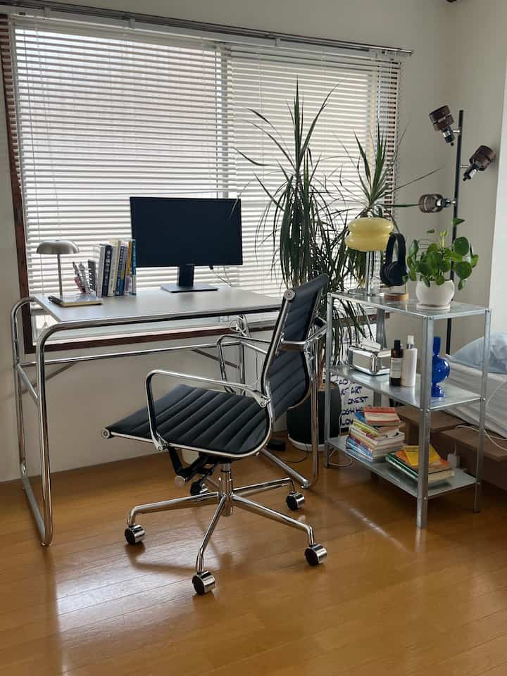 白を基調としたホームオフィス、アルミフレームのデスクと黒のオフィスチェアが配置された洗練されたモダンなインテリア