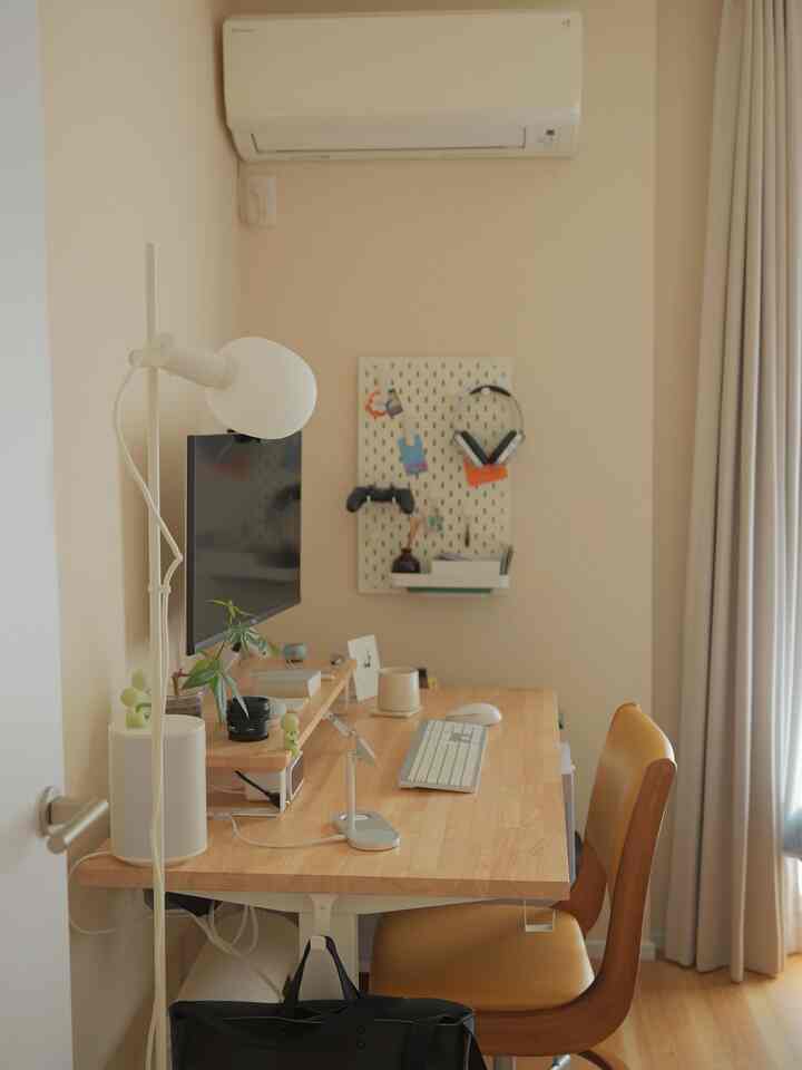 Beige and wood tone natural modern home office space featuring desk with computer and lamp, cozy work environment