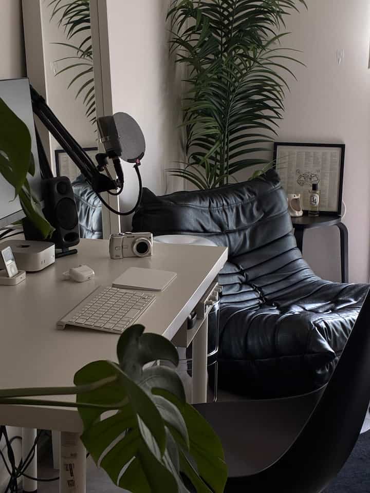 Monotone toned home office featuring a white desk, black leather chair, and a green plant creating a cozy atmosphere