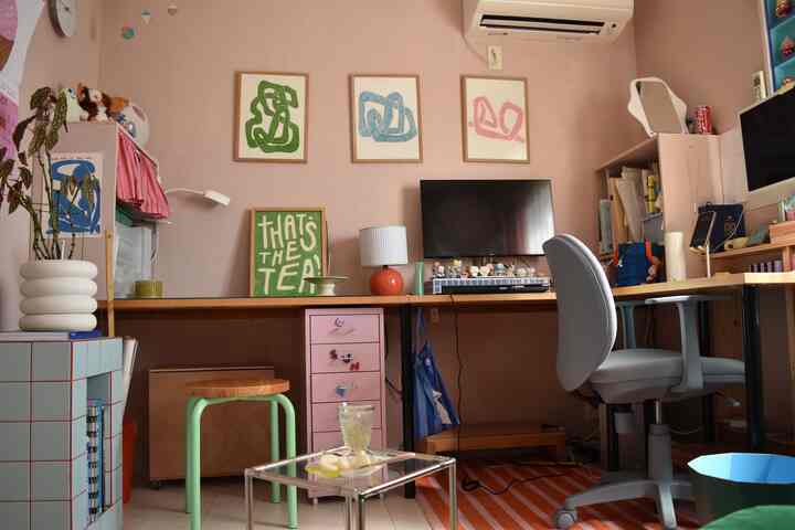 Home office space with pink walls and wooden desks, featuring chairs, stool, and posters creating a cozy, functional atmosphere