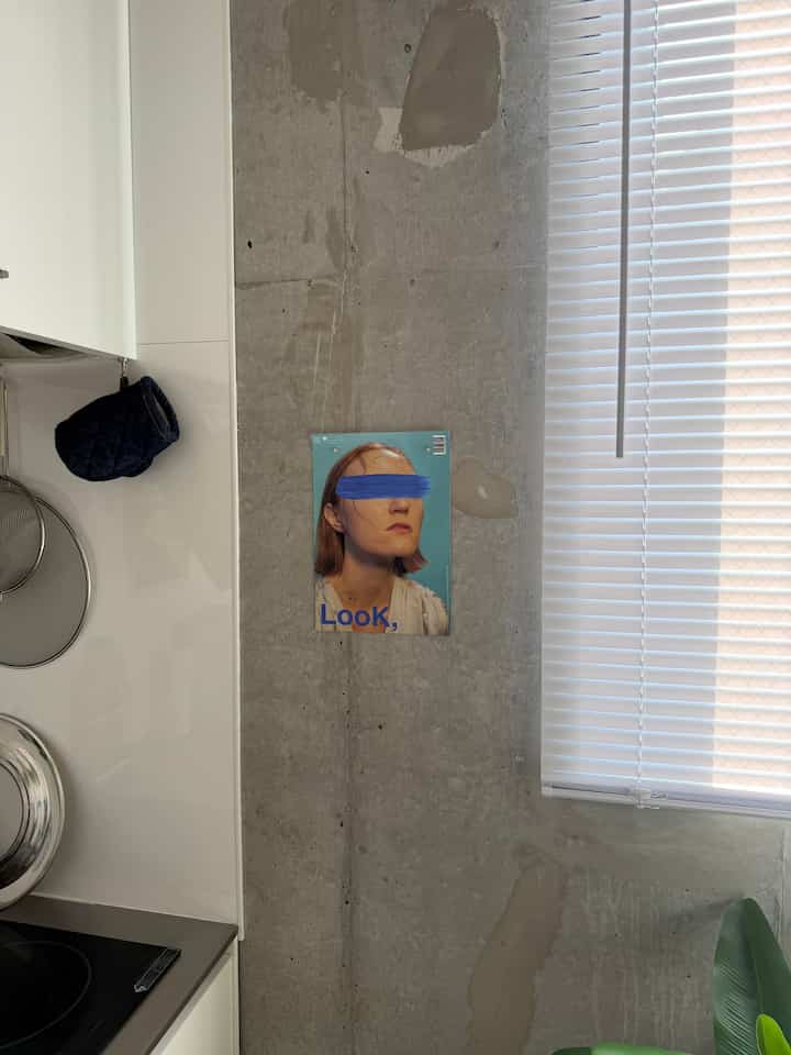 Modern and simple space featuring a concrete wall with a poster, white kitchen cabinets, and blinds
