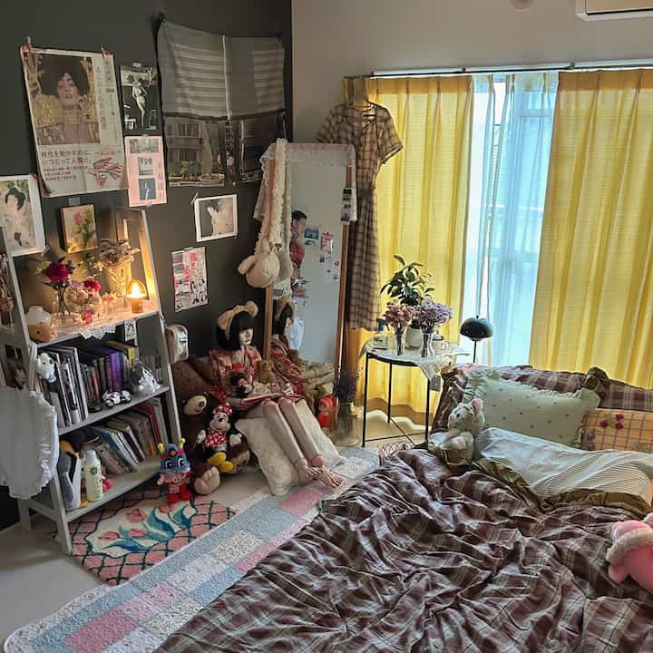 黄色のカーテンとベッドがある居心地の良いワンルーム寝室、壁のアートと様々な人形が配置された雰囲気のあるインテリア