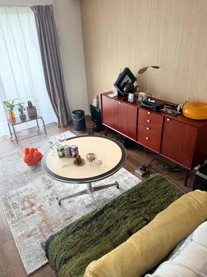 Natural-toned living room with retro furniture, featuring a round table and red storage cabinet centrally arranged in a cozy space