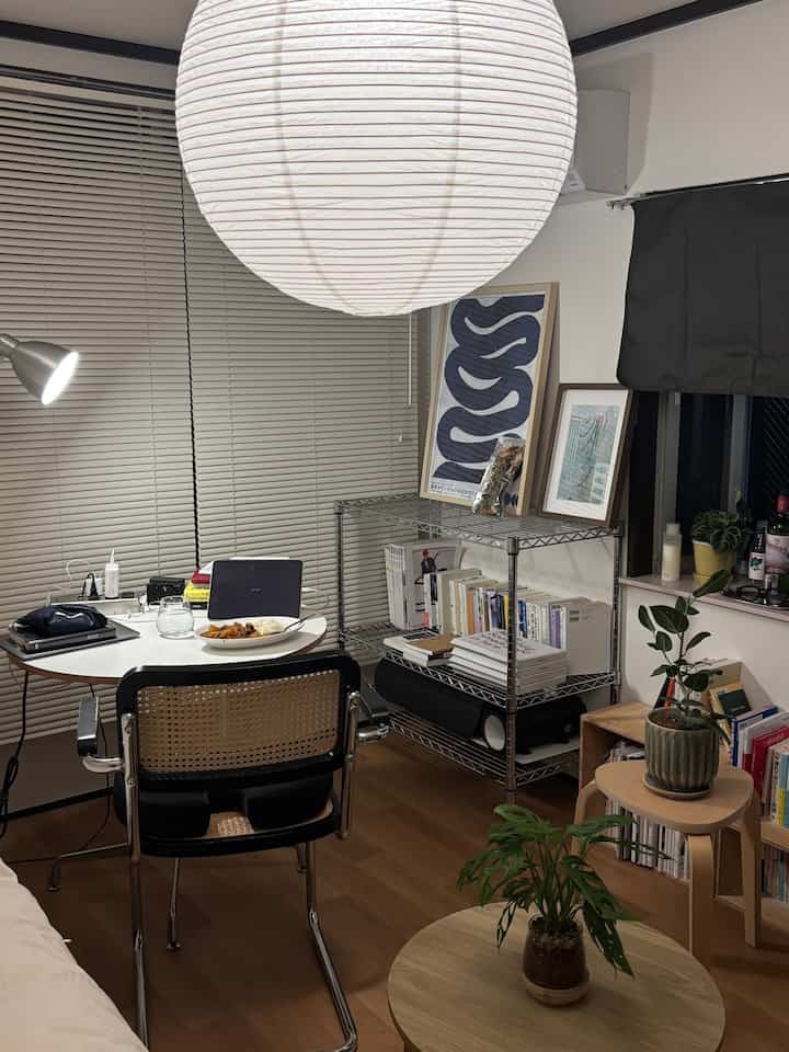 Natural modern tone studio living space with desk, floor lamp, bookshelf, and plants arranged for cozy atmosphere