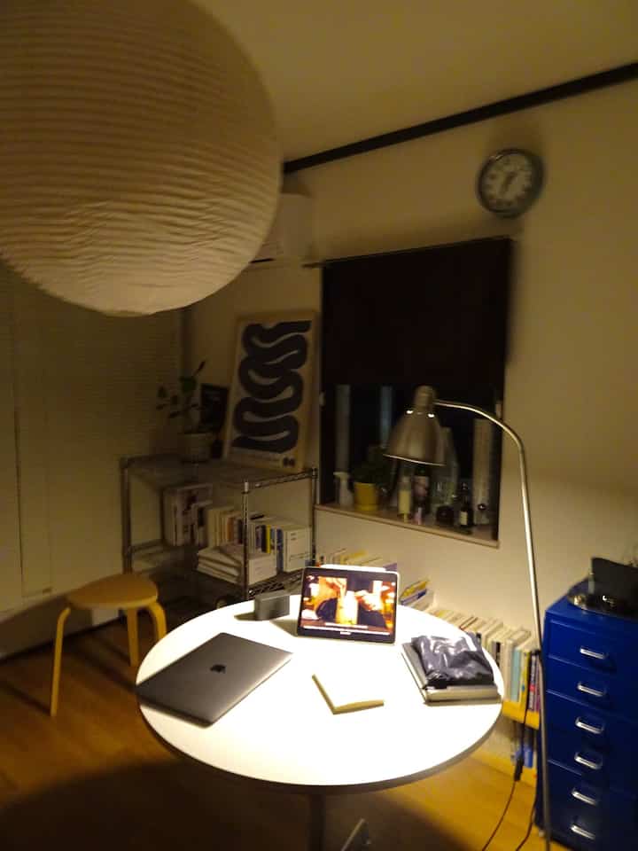 White and wood tone compact studio apartment featuring a minimalist home office with laptop and stool