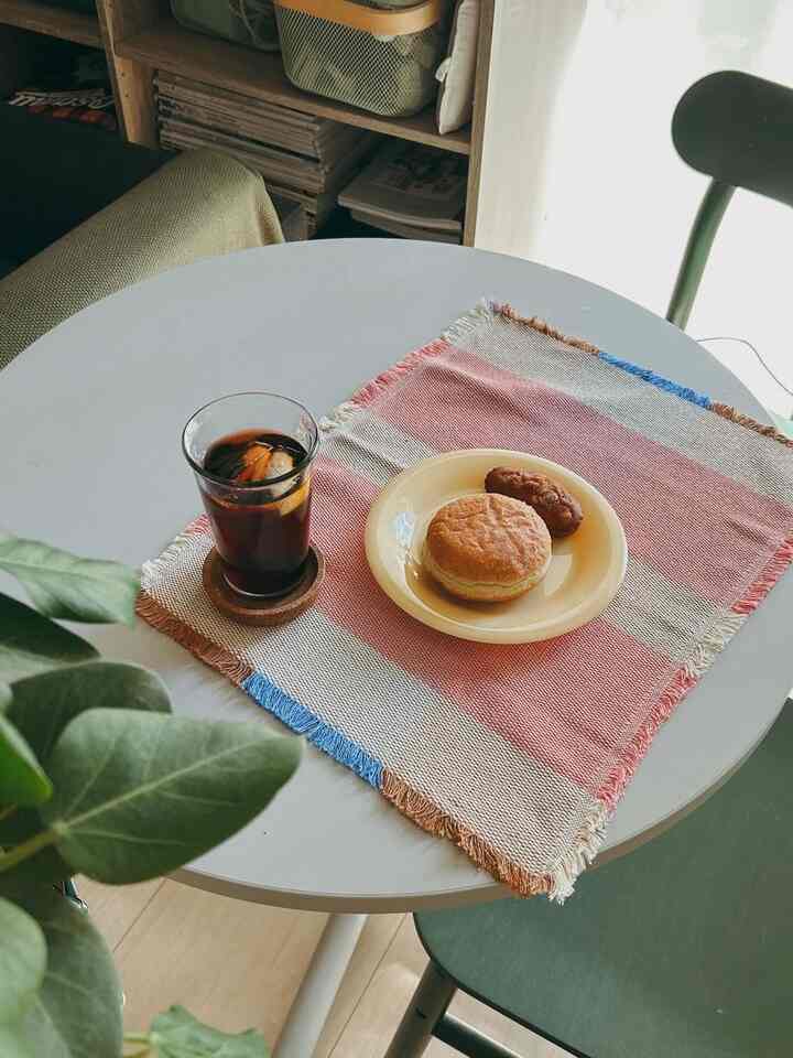 Bright white round dining table featuring colorful striped placemat, drink and dessert in a cozy single household dining space