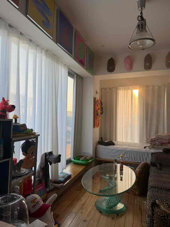 Natural wood tones and warm sunlight fill this studio apartment living and bedroom, featuring colorful posters and eclectic decor creating cozy ambiance