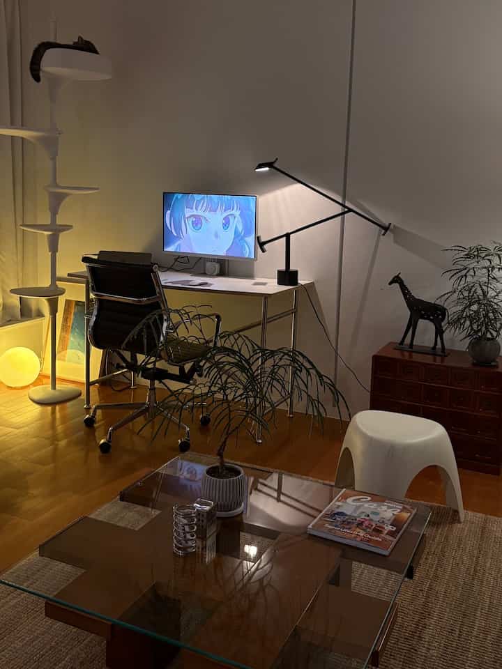 Modern home office and living room featuring brown wood flooring, white furniture, plants, and a cat tower creating a cozy atmosphere