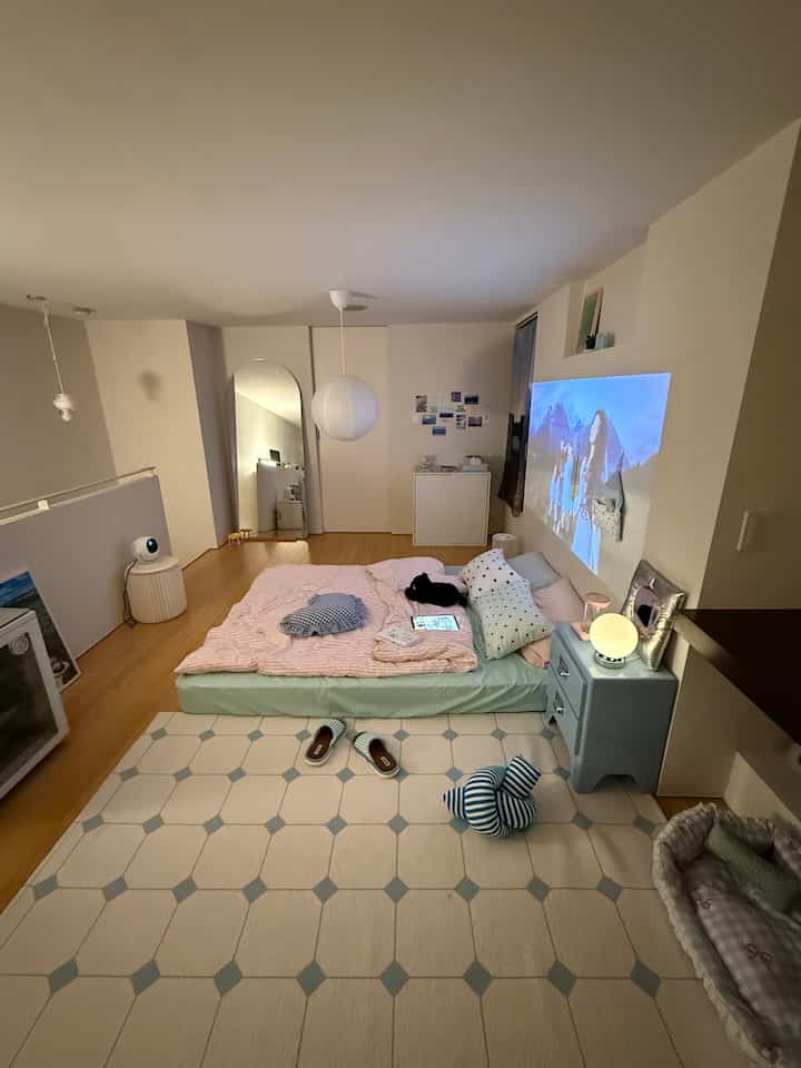 Naturally toned bedroom with soft lighting featuring low minimalist bed, a cat, and a wall projector creating cozy atmosphere