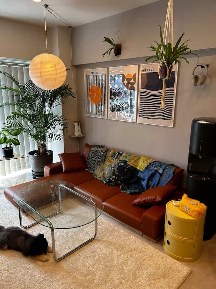 Natural color toned living room featuring brown sofa, white pendant lamp, and Art Deco posters on wall, creating a cozy atmosphere