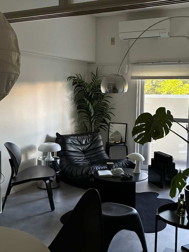 Modern living room with white walls and ceiling backdrop, featuring black leather sofa, metallic arc floor lamp, and green plants