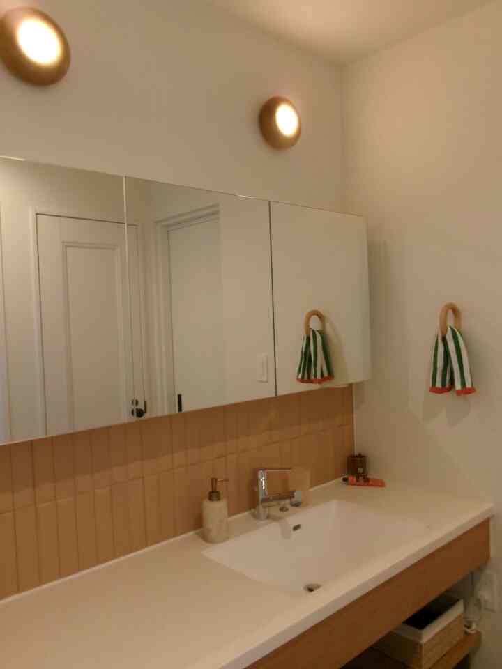 White and brown toned bathroom featuring wall sconces, mirror cabinet, and towel rack with a clean, natural atmosphere