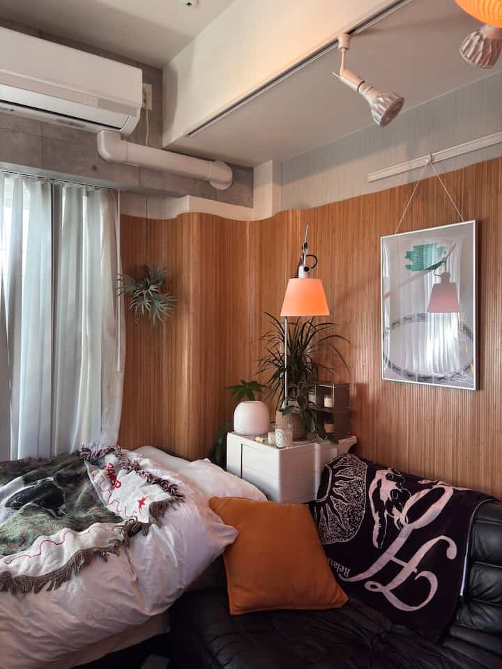 Natural wood-tone wall and white bedroom space featuring black sofa with orange cushion in a cozy room