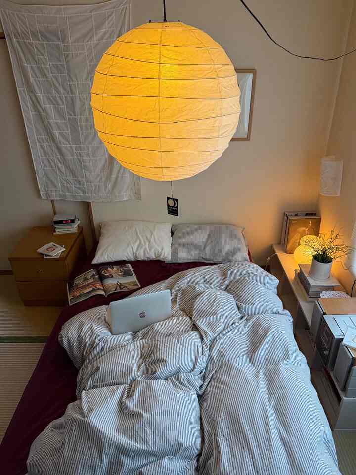Soft beige and white toned bedroom featuring a centrally placed bed and a warm glowing ceiling lamp creating cozy atmosphere