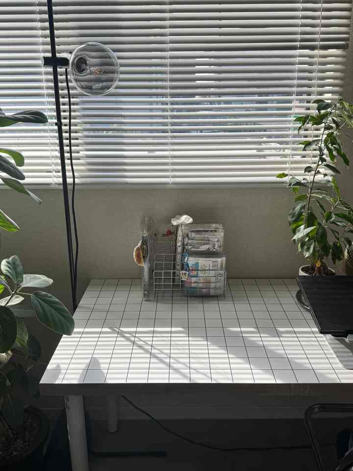 Simple modern home office with white blinds and tiled desk, featuring plants on both sides