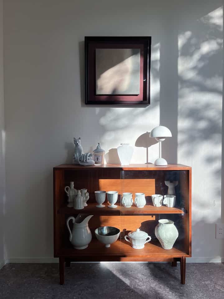 A natural, clean space with a wood-tone cabinet and white ceramics arranged under framed wall art