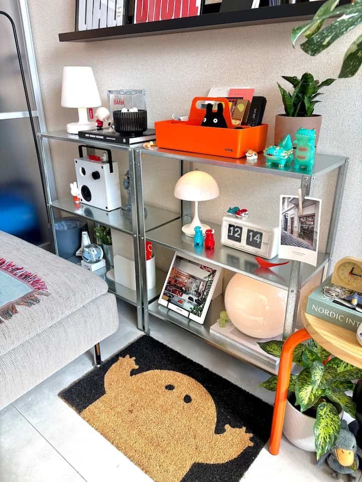 Modern living room corner in gray and white tones featuring objets, table lamps, and plants in a neat display