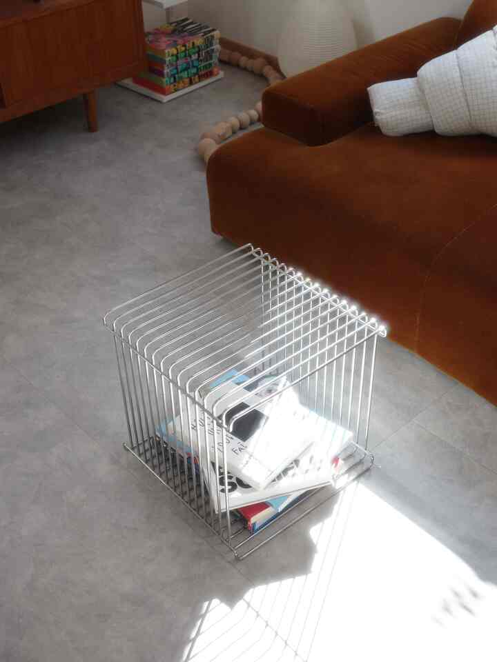 A modern gray-toned living room featuring a brown sofa and metallic wire shelf with natural lighting