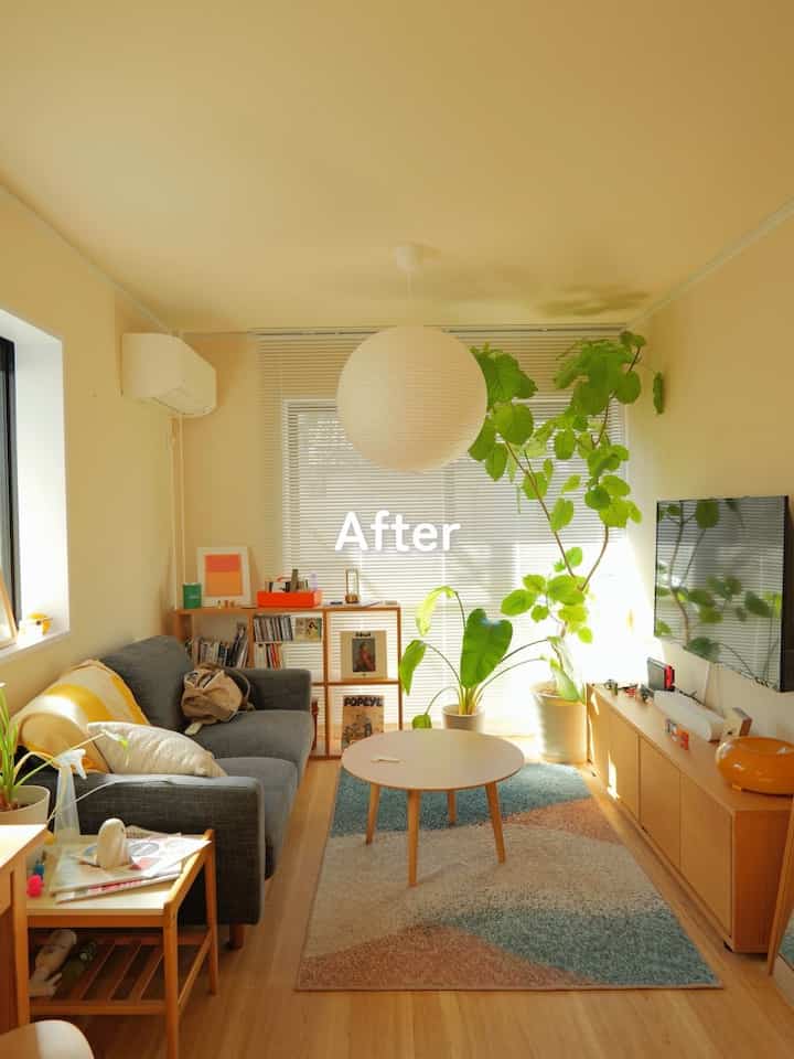 Bright, natural two-person living room with wood tones and white walls, featuring a simple sofa, round coffee table, and several green plants creating a cozy atmosphere
