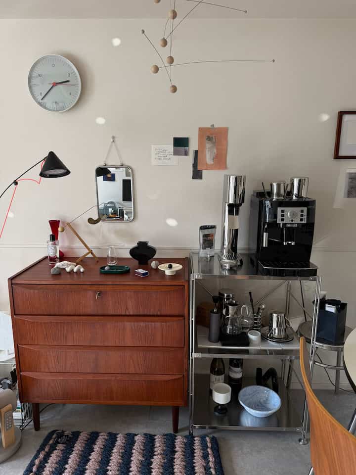 Natural-toned compact space featuring vintage furniture, stainless steel shelf, and a coffee machine creating cozy home cafe atmosphere