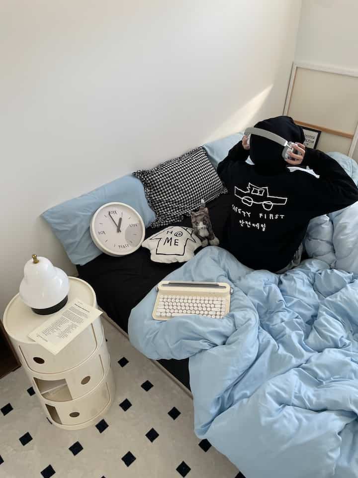 Sky blue bedding in a bedroom with white walls, person wearing black hoodie sitting on the bed