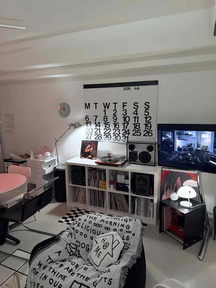A modern and cozy Korean interior living room with white and black tones, featuring a large calendar and a record player