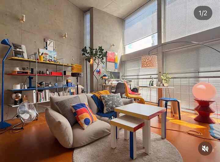 Cozy living room with warm orange flooring and concrete walls for a single household, featuring natural light and colorful furniture accents