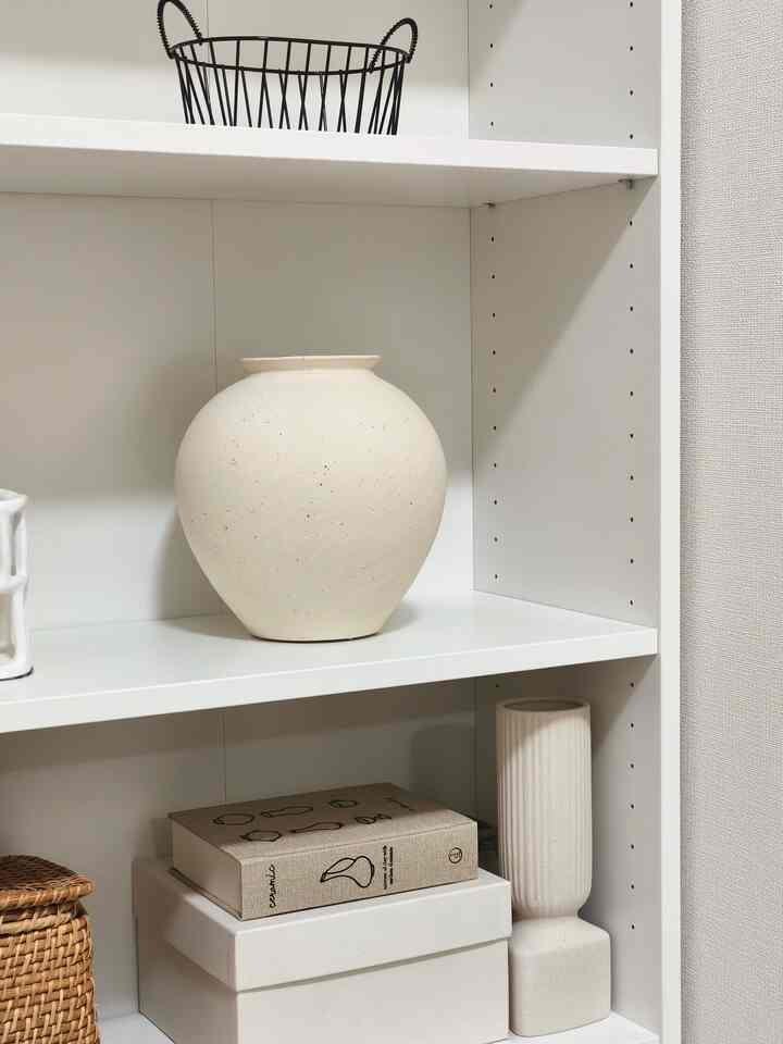 白を基調とした棚にナチュラルなラタンバスケットとテクスチャードセラミック花瓶が配置されたシンプルで落ち着いた印象のインテリア