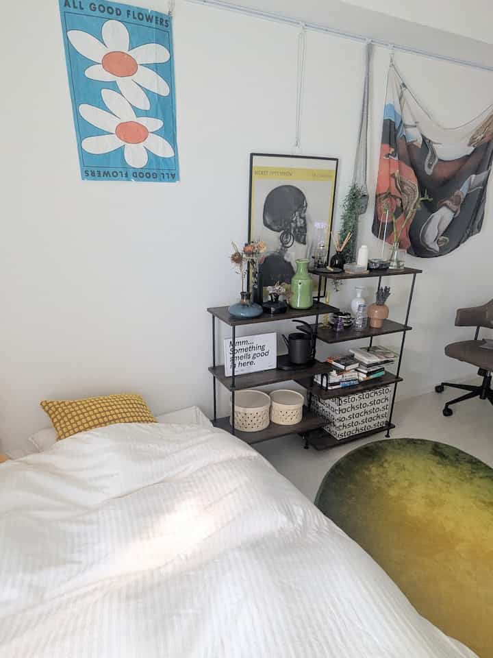 白と緑のトーンの寝室、整った寝具とポスター、棚が配置された雰囲気のある空間