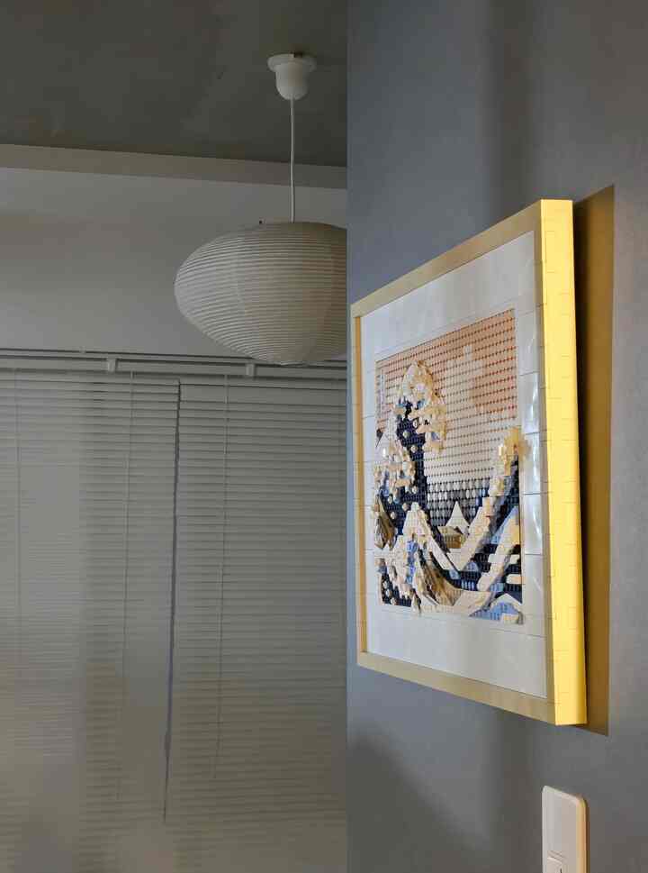 グレーの壁と白いペンダントライトがある寝室、壁にLEGO製の北欧風アート作品が掛けられた空間