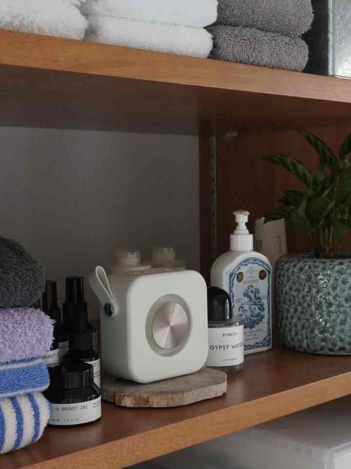 木目調の棚に折りたたまれたタオル、ディフューザー、化粧品ボトル、観葉植物が配置された整ったバスルーム収納スペース