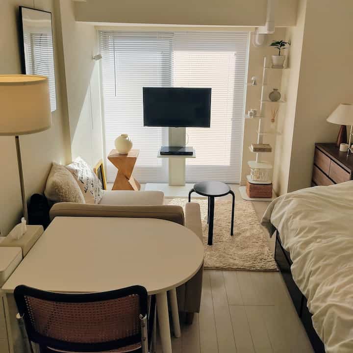 Natural-toned 1K studio apartment for single household featuring bed, sofa, TV, and stool in a cozy setting