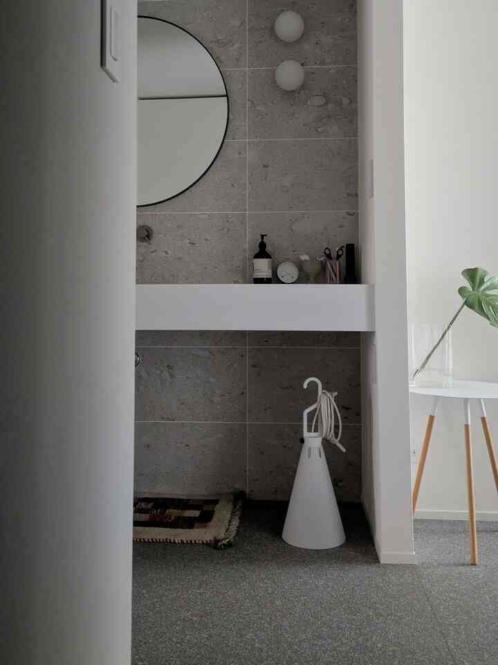 グレー調の壁とホワイトの浮き棚、丸い鏡がある縦長のモダンな玄関空間