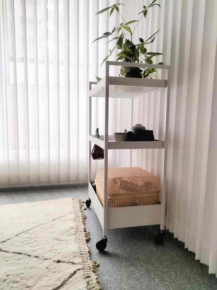 白とナチュラルの色調のリビング、隙間収納用の白いメタルカートと植物が配置されたすっきりとした雰囲気のインテリア