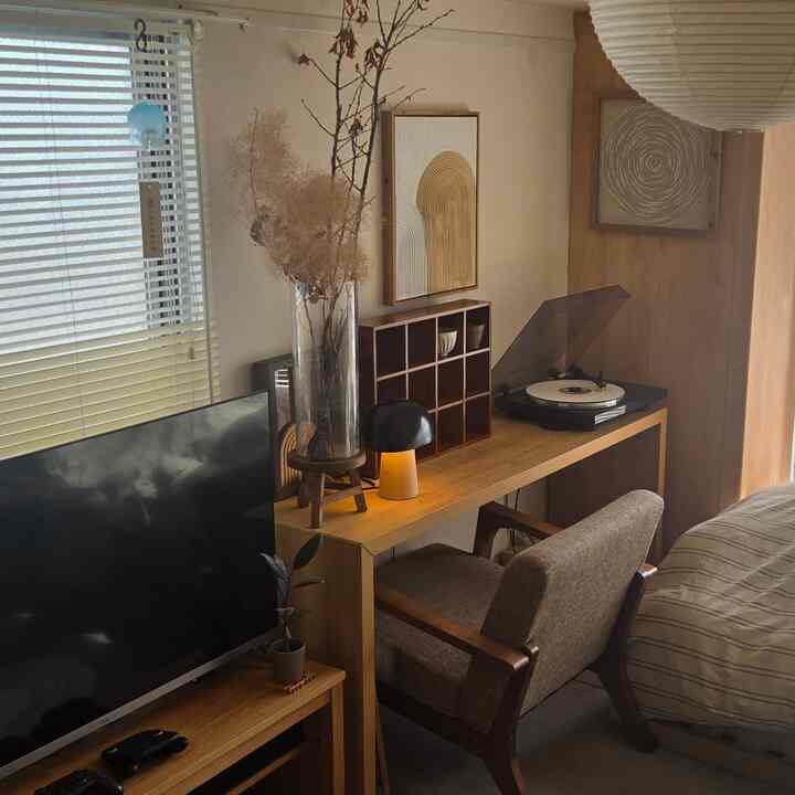 温かみのある木目調と北欧スタイルのワンルーム、デスクとターンテーブルが配置された雰囲気のあるホームオフィス空間