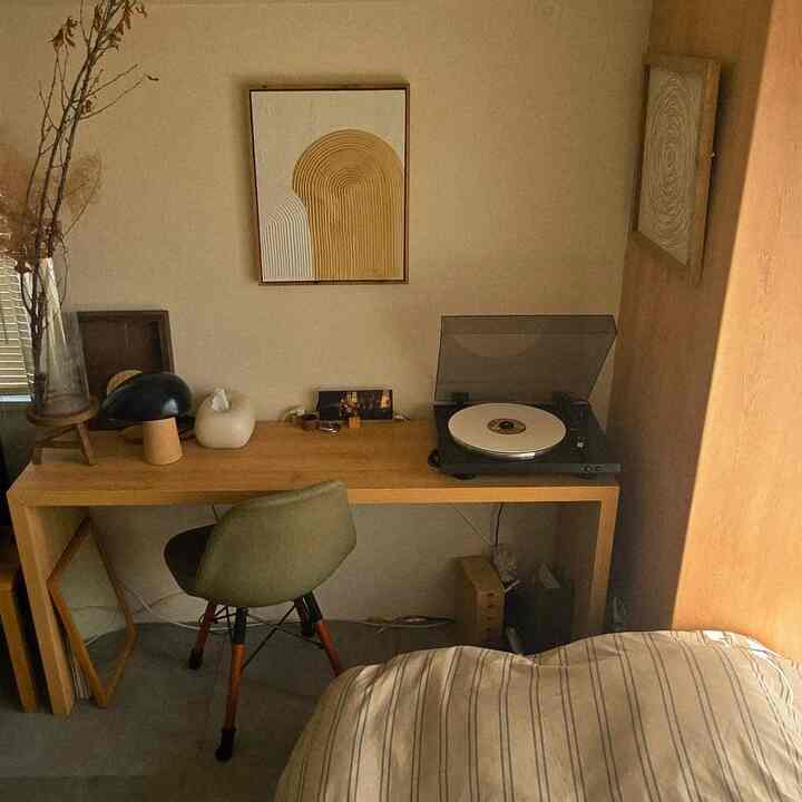 Natural toned small bedroom featuring a wood tone desk with green chair and art panels on the walls, creating a cozy atmosphere